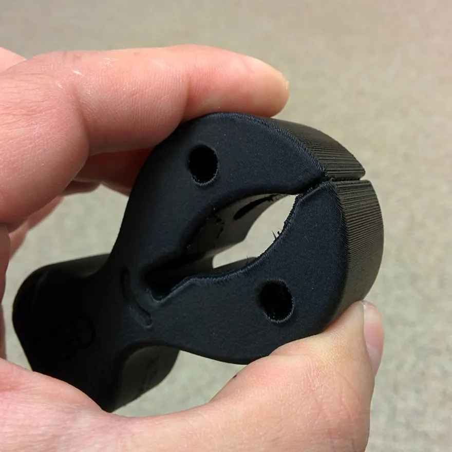 A flexible black part printed in TPU filament, flexed between fingers